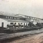 Pendant la Première guerre mondiale, la compagnie magnymontoise Les Usines générales de char set de machineries limitée obtient un volumineux et lucratif contrat du gouvernement fédéral afin de fabriquer des coquilles d’obus destinées à l’Armée impérial Britannique. Les installations initiales de Les Usines générales de chars et de machineries limitée. Ce bâtiment sera la proie des flammes en 1916. La photo est probablement prise avant 1915, puisque nous y apercevons des machines à vapeur servant aux travaux de voirie.